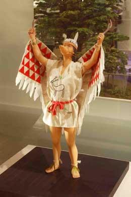 赤と白の鳥のような翼をつけて手を上げるシャーマンの模型の写真