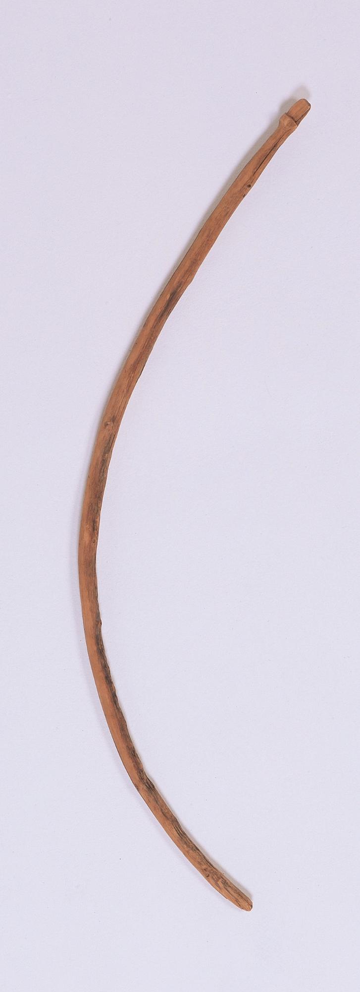 木製の弓の写真。一木でできており、中央から大きく湾曲する。両端が薄く削り出され、弭と考えられる。